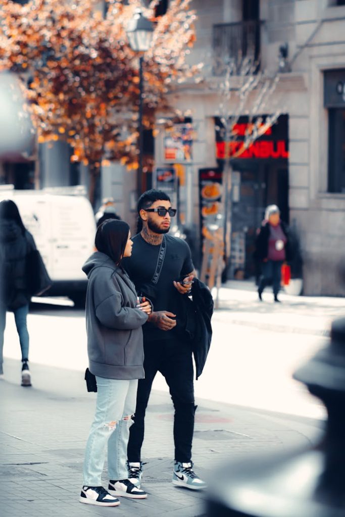 Stylish couple walking on an urban sidewalk during autumn, showcasing modern street fashion.