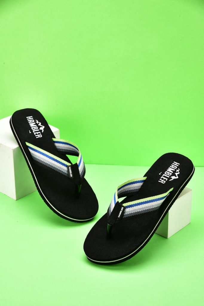 Modern black flip flops displayed against a bright green backdrop in a studio setup.